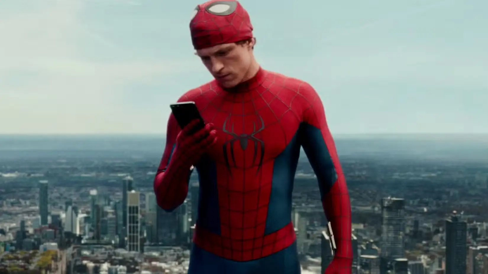 Tom Holland's Spider-Man with his mask up and looking at his phone in Spider-Man- Brand New Day